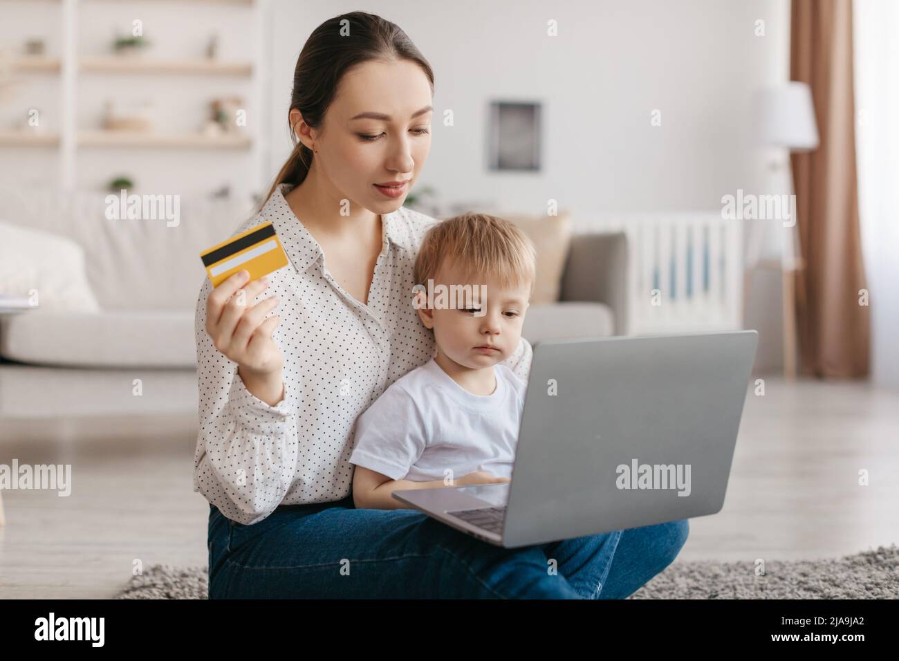 Pretty young mother with toddler baby using laptop and credit card shopping online ordering toys or clothes from home Stock Photo Alamy