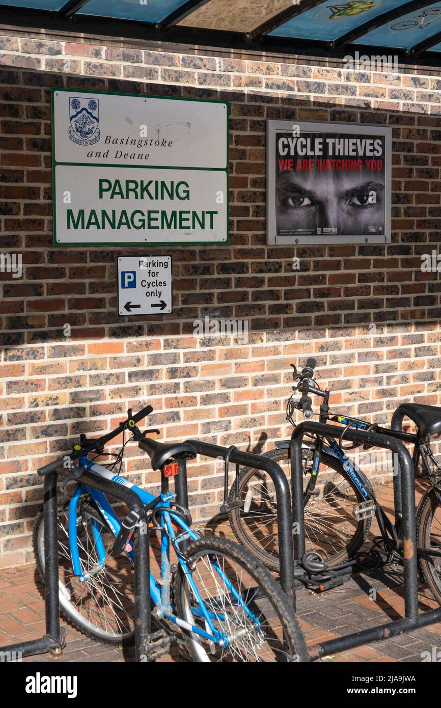 A Basingstoke council bike shelter with a bike rack and bicycles and a poster warning 'Cycle thieves we are watching you' with a pair of eyes. UK Stock Photo