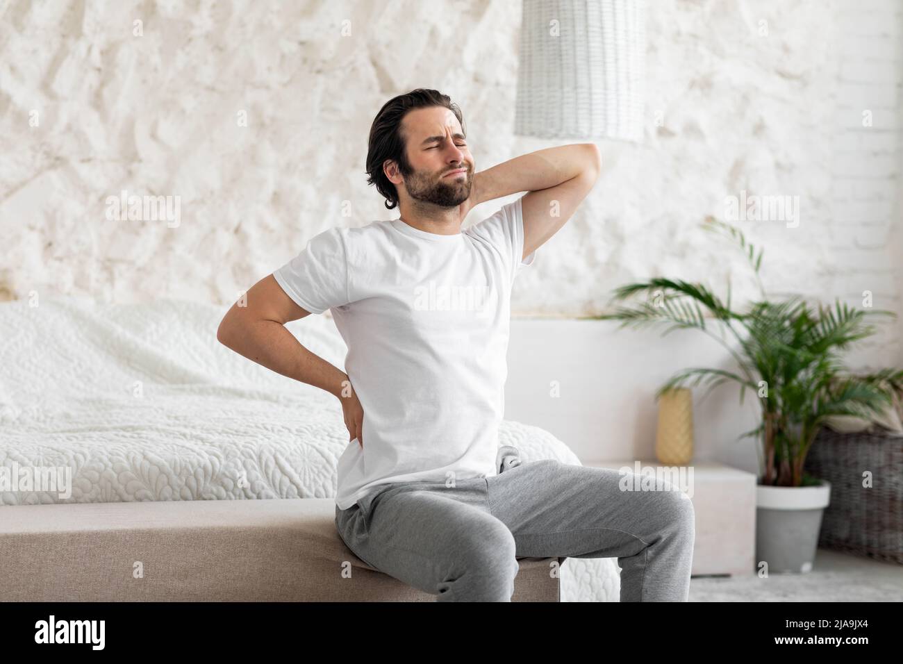 Unhappy man suffering from back pain at home in bedroom Stock Photo - Alamy