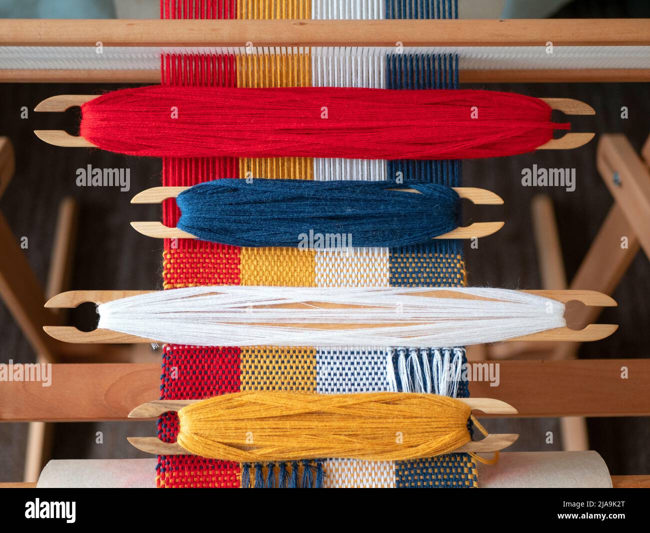 Four shuttles with yarn of different colors on the loom. Weaving shuttles with blue, white, red and yellow threads on the weaving project Stock Photo