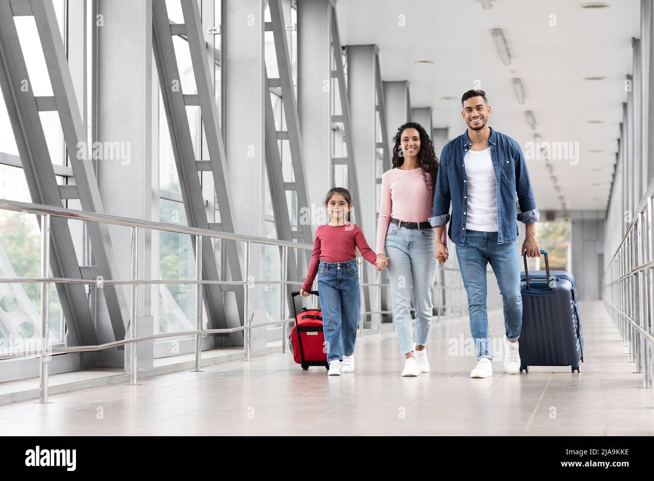 Travel Insurance. Smiling Arabic Family With Daughter Walking With Suitcases At Airport Stock Photo