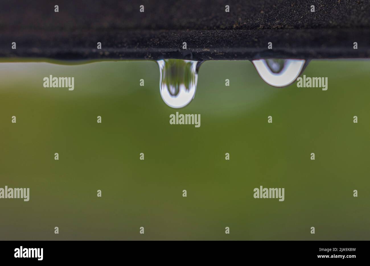 Macro view of falling raindrops from window frame of skylight during