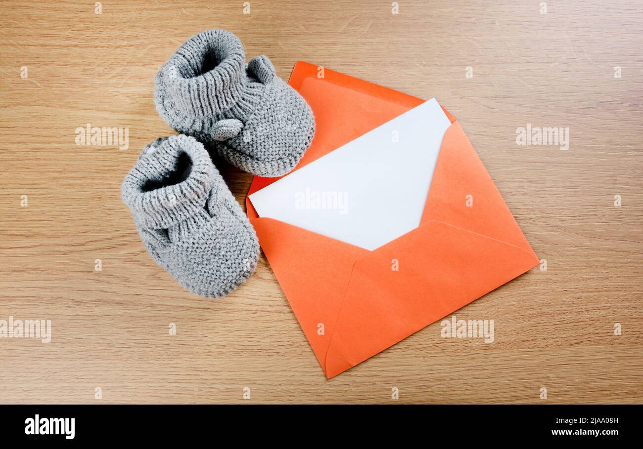 Gray baby bootees with a empty paper in a orange envelope on table Stock Photo