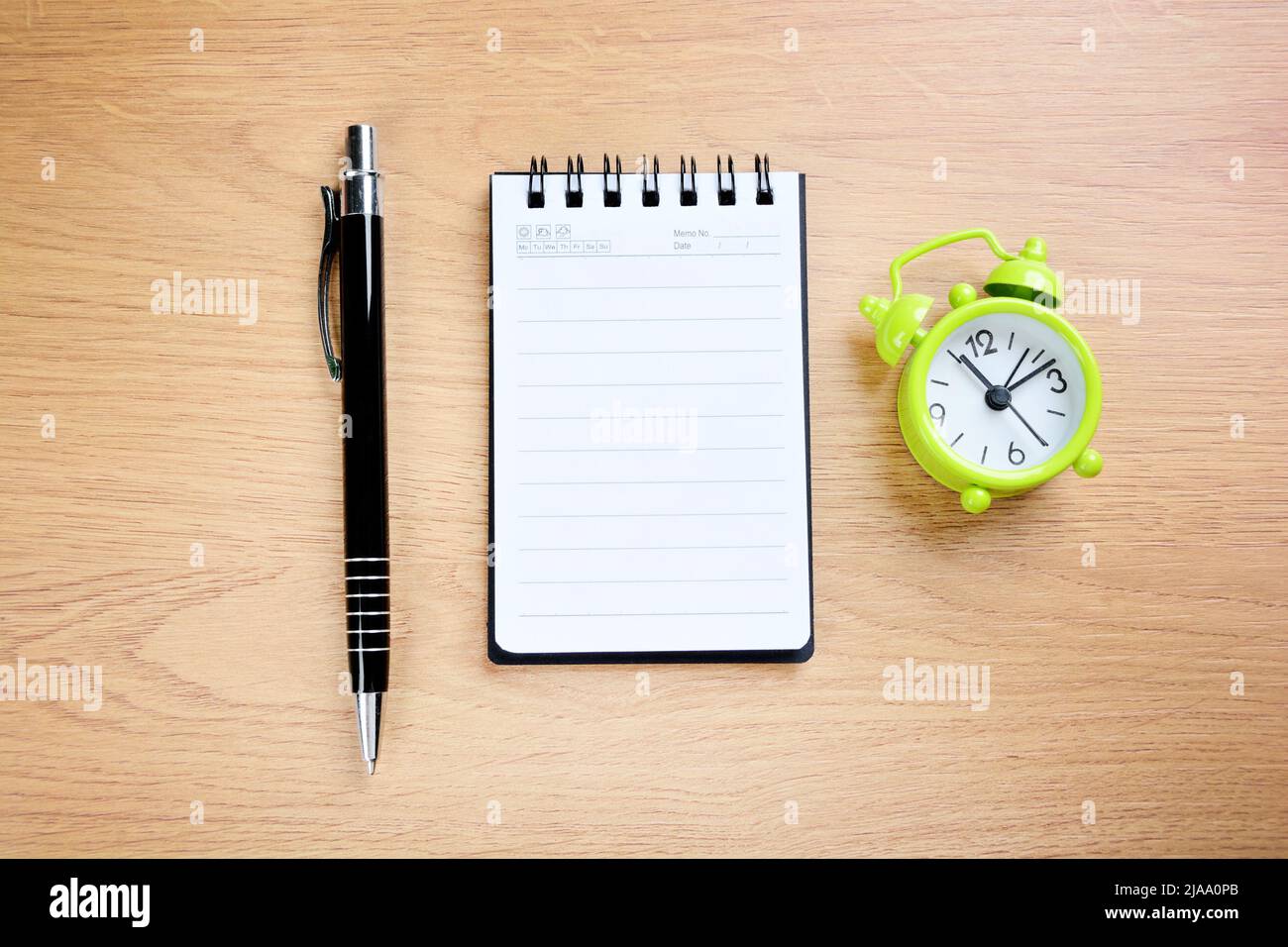 Green alarm clock with office pen and empty notebook on a wood table Stock Photo