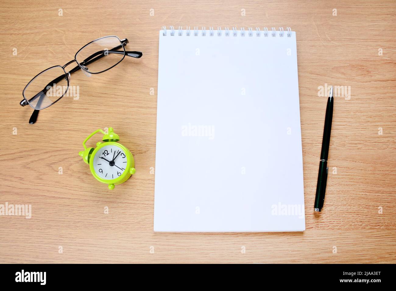 Empty notepad with alarm clock, pen and eyeglasses on wooden table Stock Photo