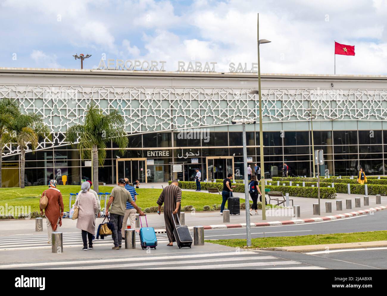 Passengers travelers with rolling luggage walking toward Rabat Sale Airport building with Moroccan flag, Morocco, North Africa Stock Photo