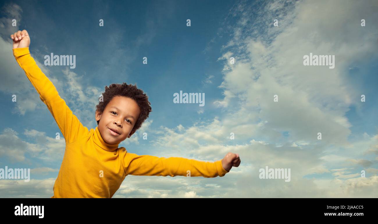 Happy joyful black kid on blue sky and white clouds background outdoors Stock Photo