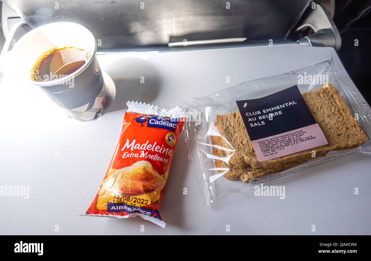 Air France airplane meal - Club emmental au beurre sandwich, Madeleine cake, coffee in plastic cup - on a seat table  in cabin in flight Stock Photo