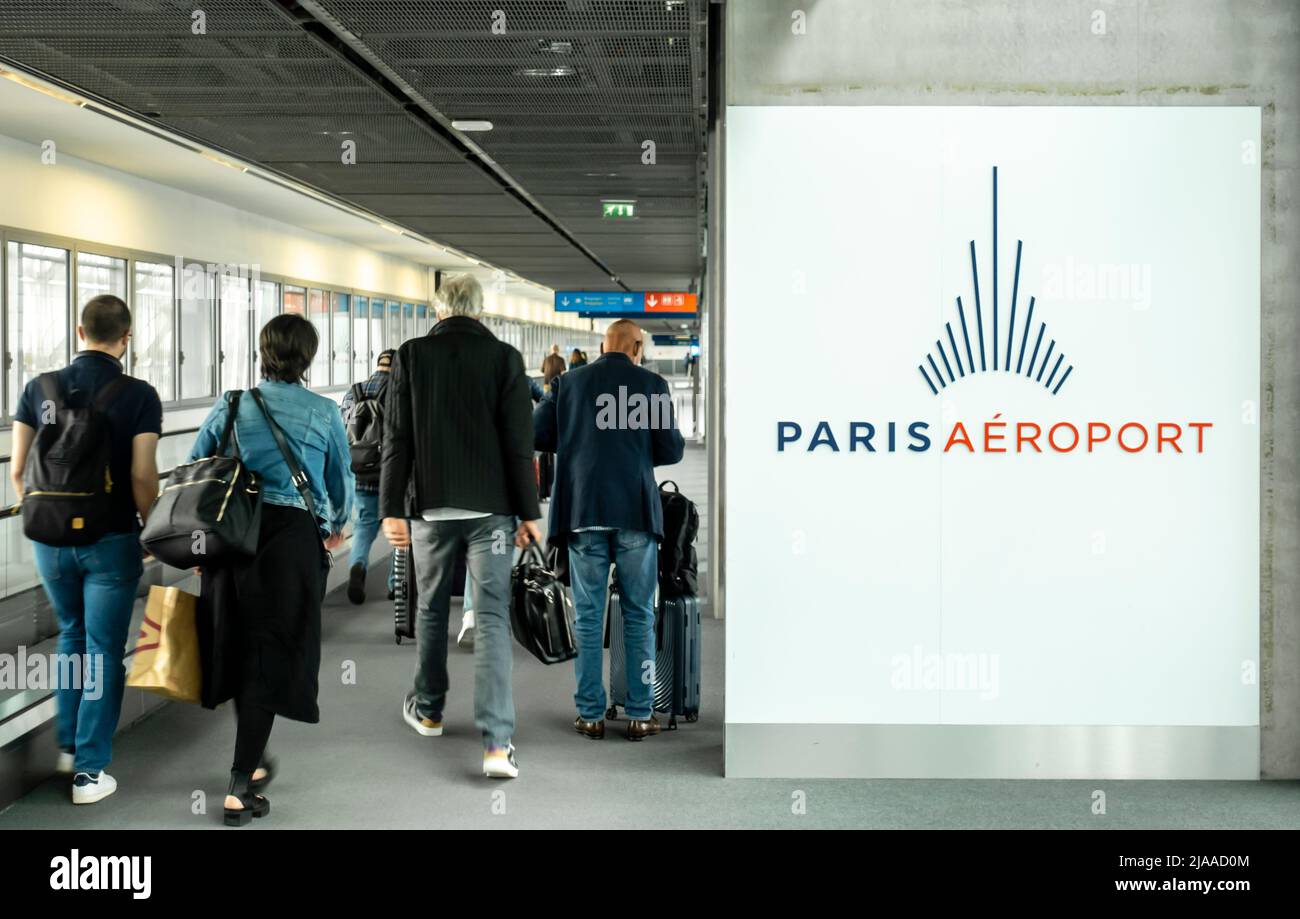 Passengers with carry-on luggage walking past Paris Airport logo and info at Transfers - connected flights -arrivals at Paris  Airport, CDG, France Stock Photo