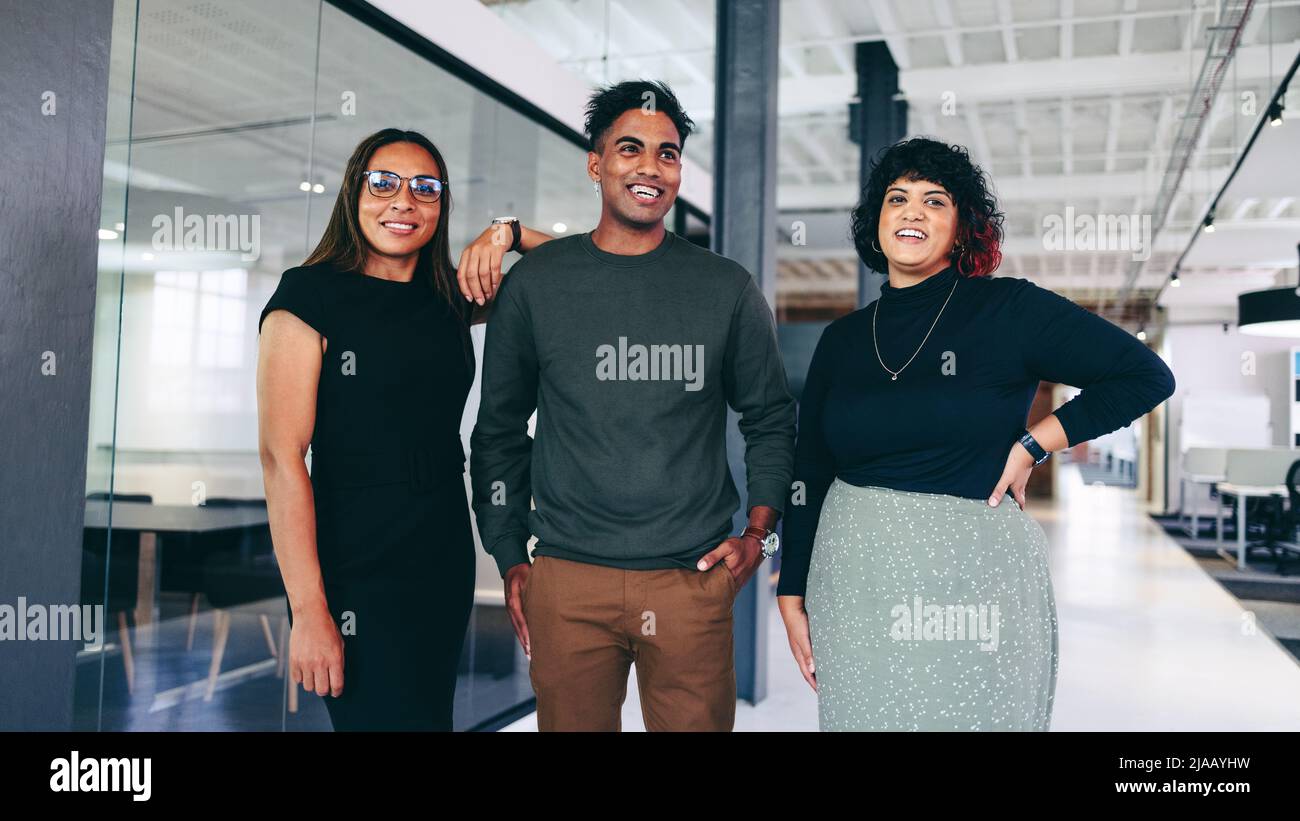 Happy team of businesspeople smiling cheerfully while standing together in a creative office. Group of three businesspeople wearing business casual in Stock Photo