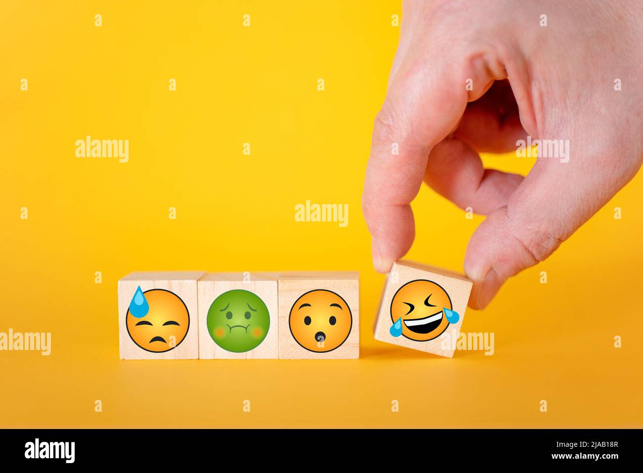 Emoji emoticons on a yellow background, the hand takes one cube with a smiley emoji. The concept of the world day of emoticons. Stock Photo