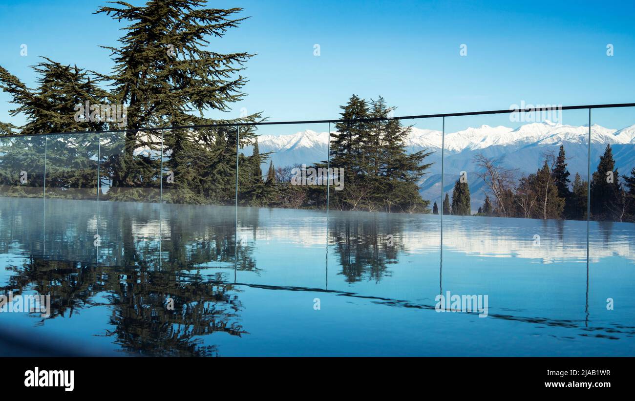 Outdoor swimming pool at the resort. Mountains landscape panorama. Snow on the tops of the mountain range. Reflection of trees and mountain peaks on t Stock Photo