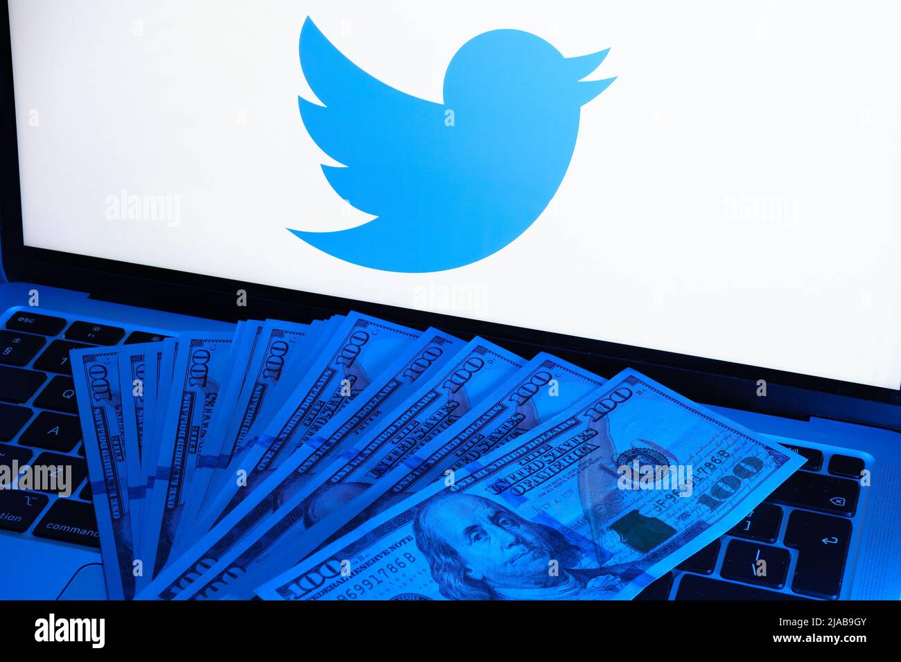 Dollar banknotes lit with a blue light placed on laptop with blurred Twitter logo. Concept. Stafford, United Kingdom, May 29, 2022 Stock Photo