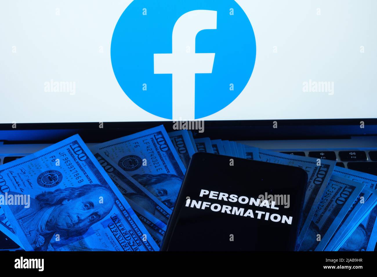 Words PERSONAL INFORMATION seen on smartphone placed on dollars and Facebook logo on blurred laptop behind it. Concept. Stafford, United Kingdom, May Stock Photo