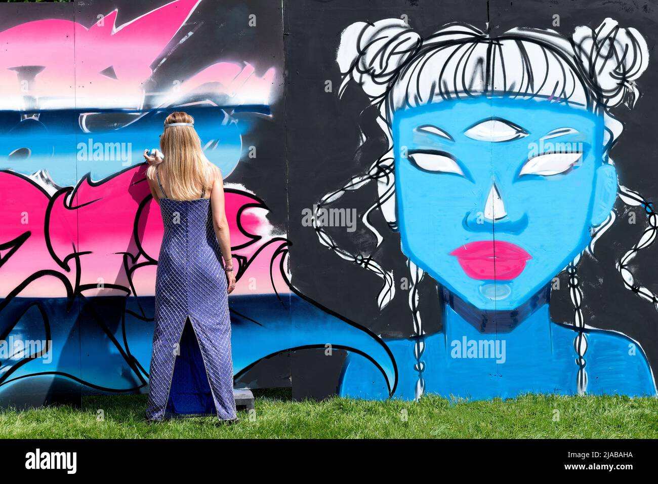 Bristol, UK. 28th May 2022. A female street artist, wearing an evening dress, works on a large mural during the Bristol Upfest street art festival Stock Photo