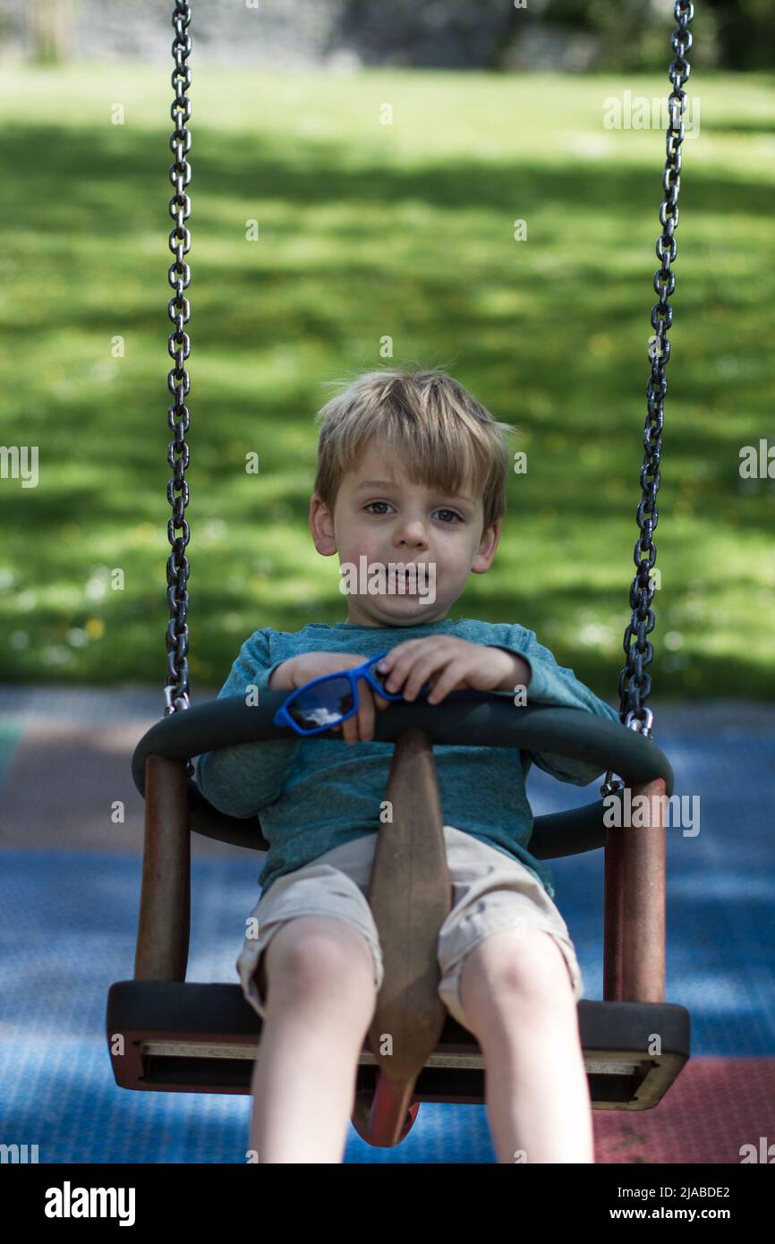 3 Year old boy plays on a swing in a park Stock Photo