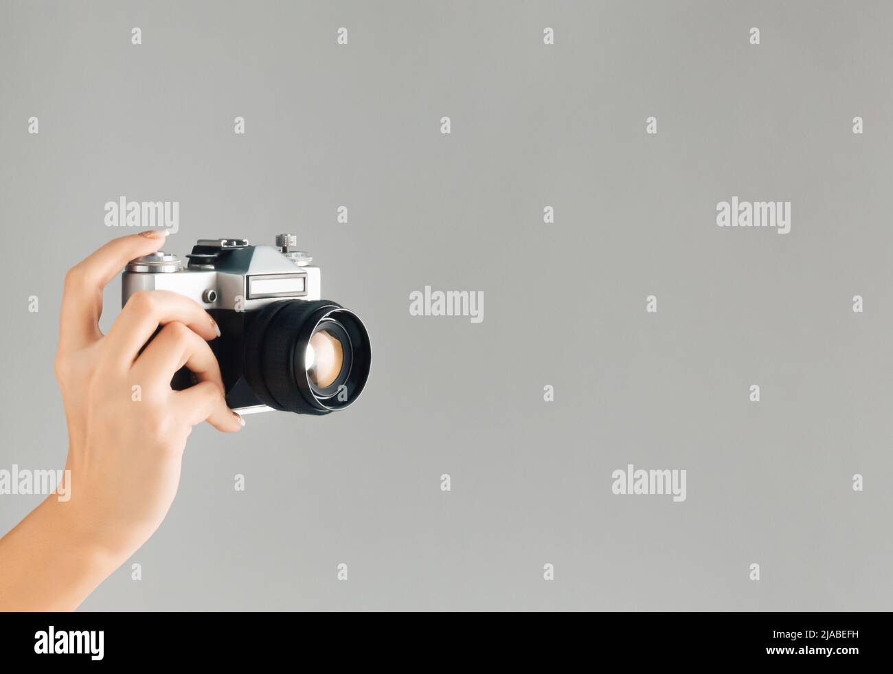 Old photo camera in woman hand on grey background with vintage color effect. Minimal retro style. Copy space. Stock Photo