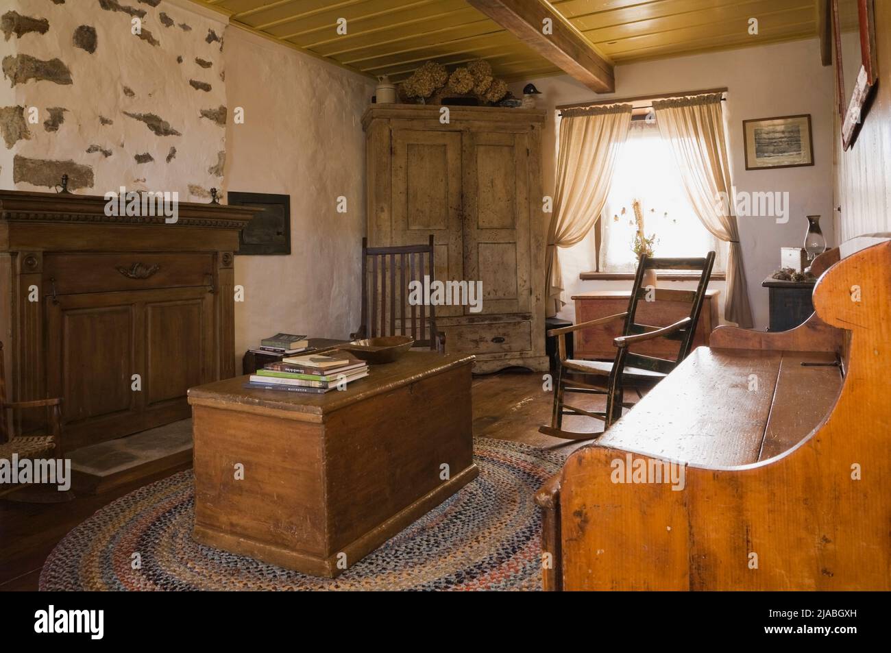Antique chests, rocking chairs, armoire and furnishings in living room inside old circa 1840 Canadiana cottage style fieldstone home. Stock Photo