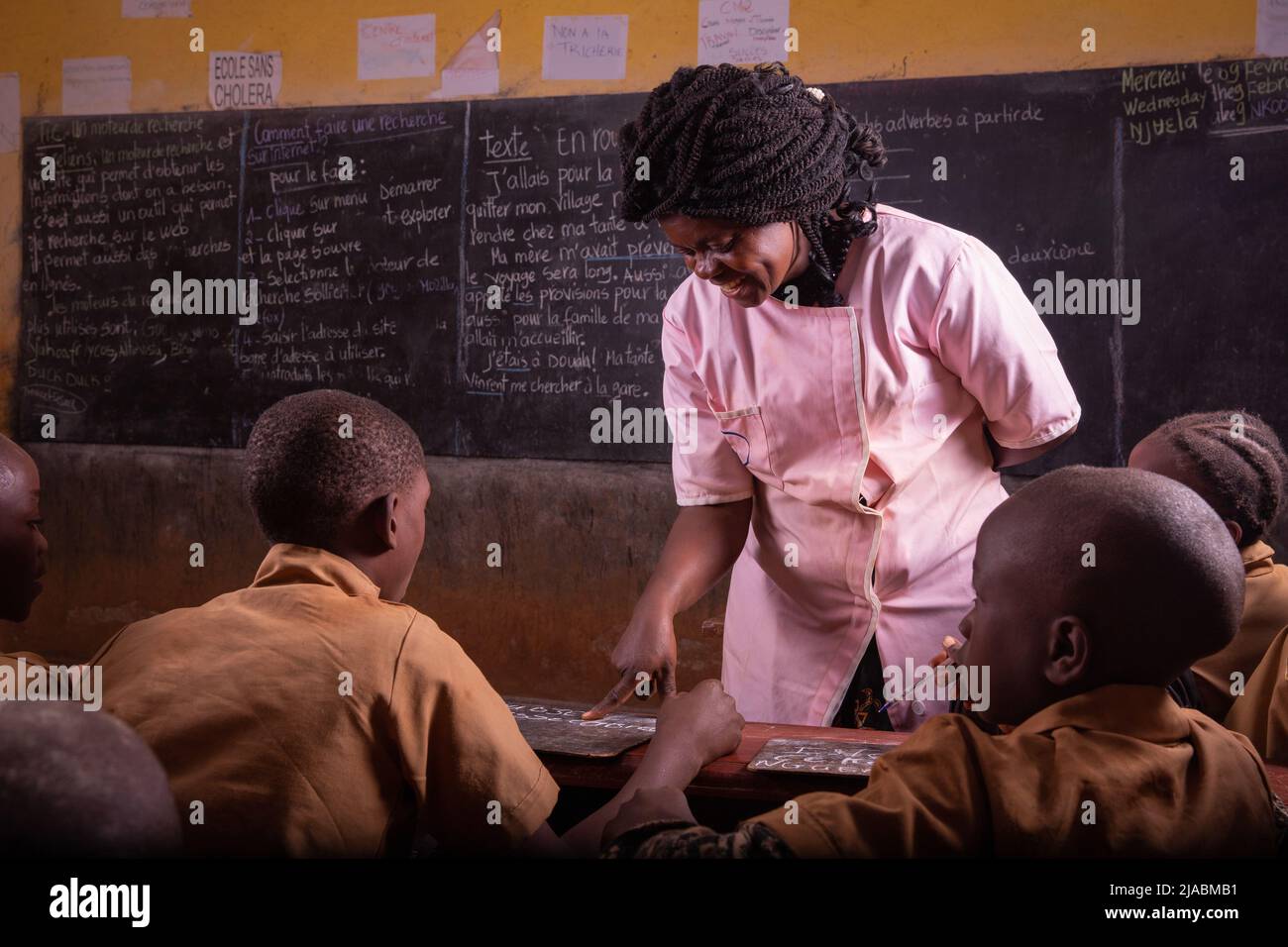 Black teacher intent on explaining writing on the black board to very attentive pupils. Stock Photo