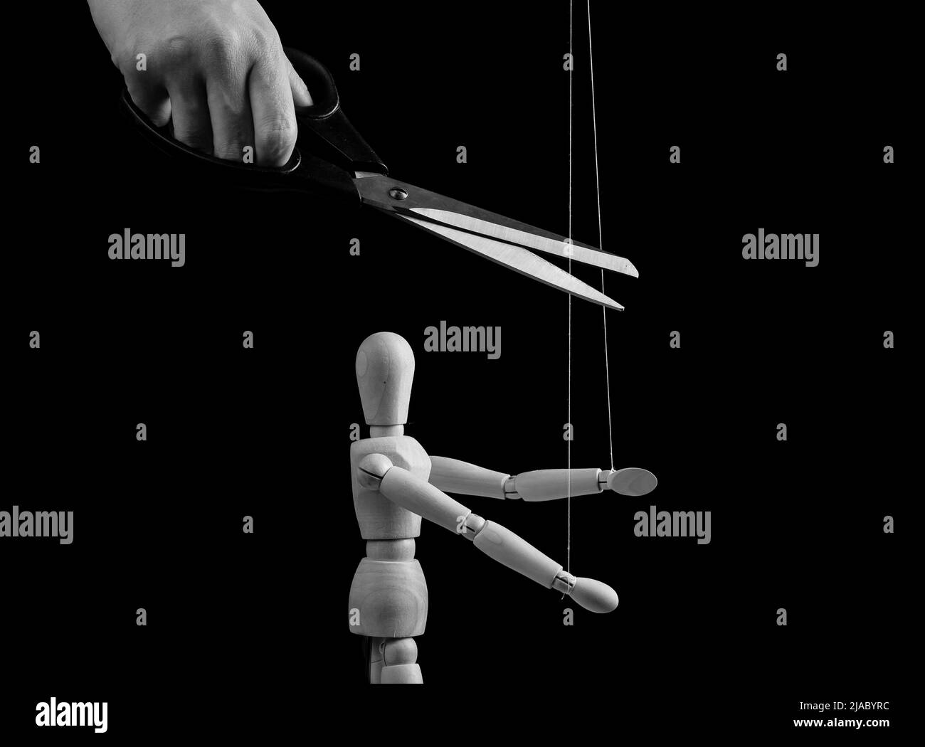 Hand cutting strings over puppet with scissors. Freedom, overcoming addiction, liberation from slavery, abuse, abusive, toxic relationship cessation concept. Black and white. High quality photo Stock Photo