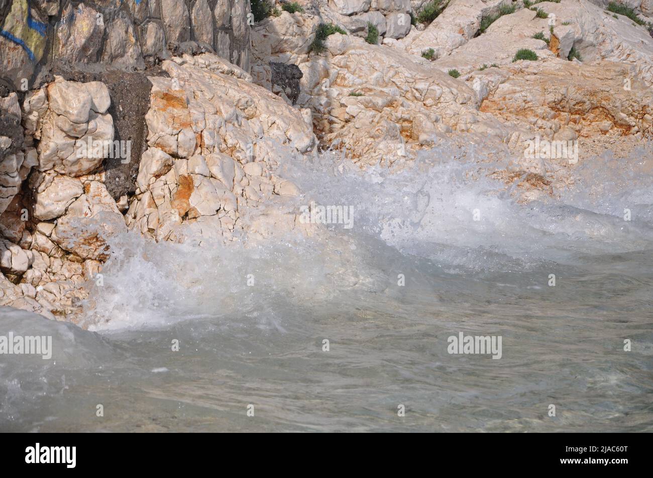 Wave splashing on a Croatian beach on early summer. Waves splashing into volcanic rocks on the coast of Rijeka beach Pecine. Stock Photo