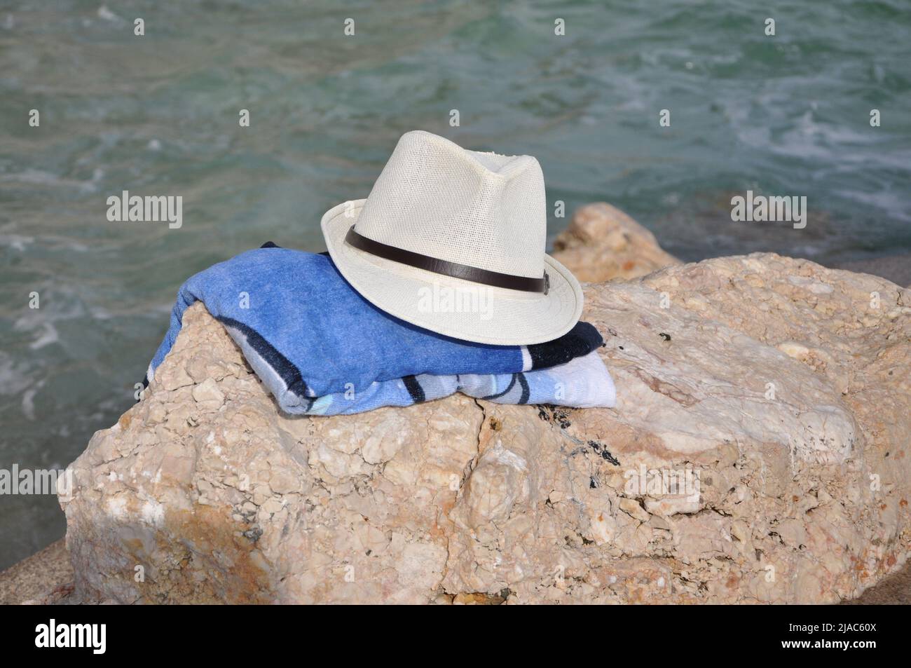 white sun hat on the tropical beach. Beach hat lying on the rocky by the sea. Hat on a towel on the beach Stock Photo