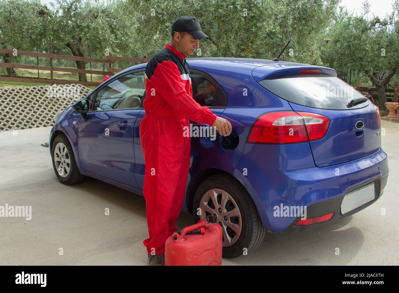 Image of a mechanic in overalls as he pours an additive into the tank of a car. Reference to expensive fuel Stock Photo