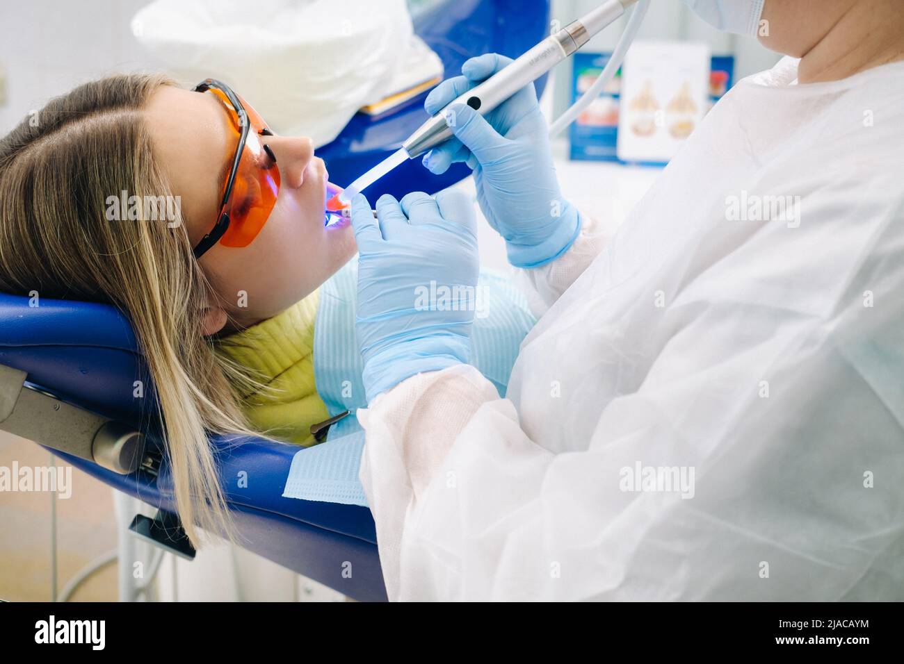 A young beautiful girl in dental glasses treats her teeth at the