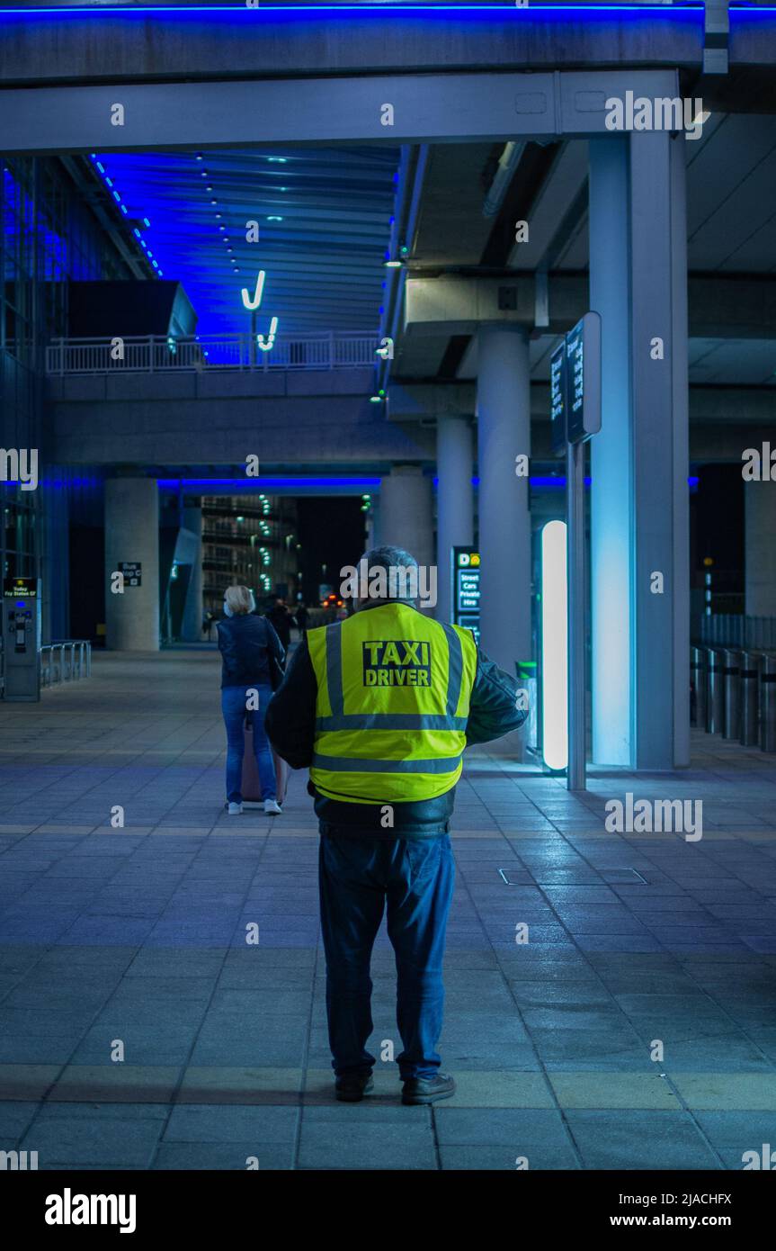 Rear portrait of a taxi-driver standing in terminal 2, Manchester Airport, waiting for customers. Stock Photo