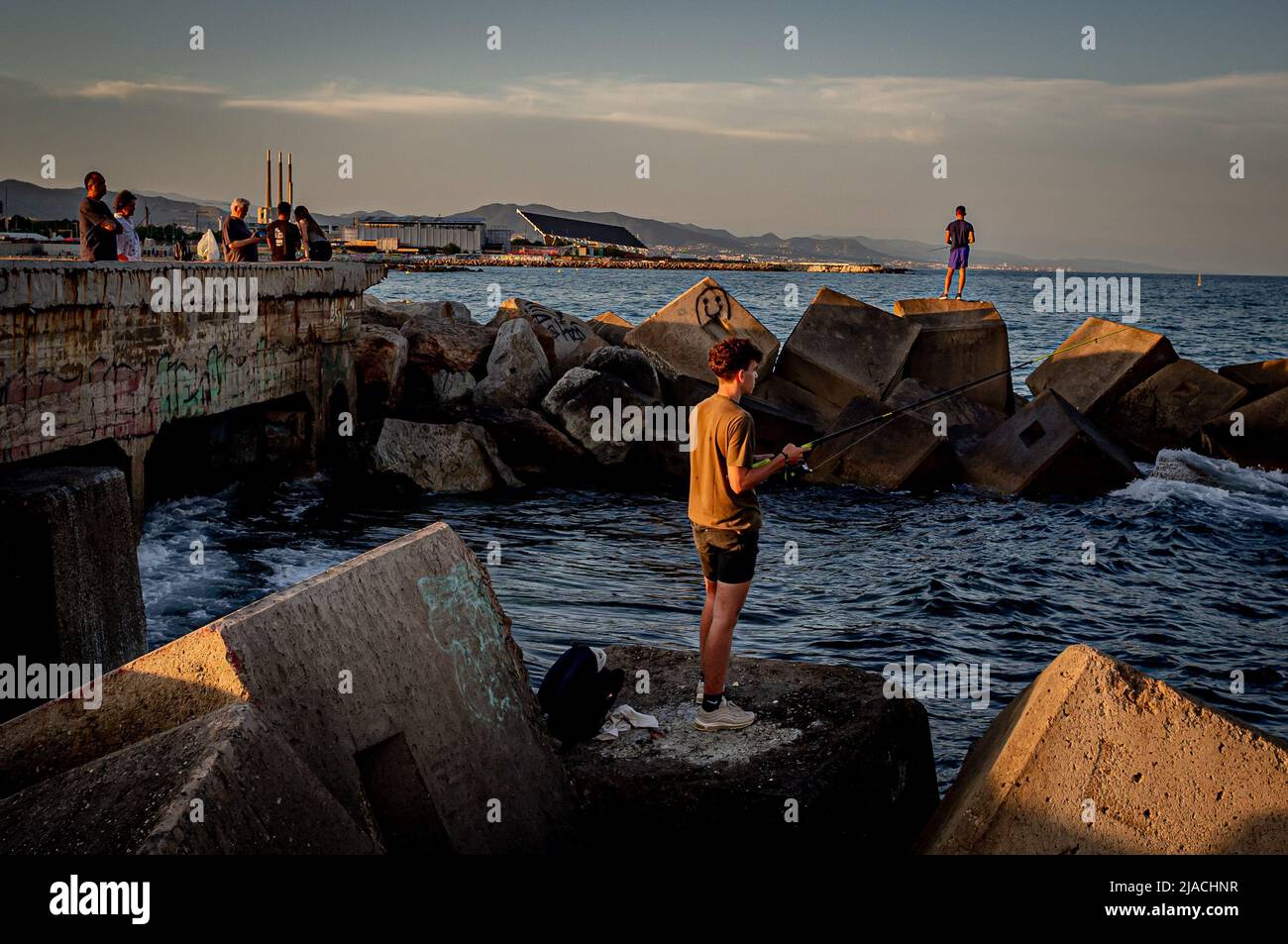Men fish from a breakwater at sunset in Barcelona. Stock Photo