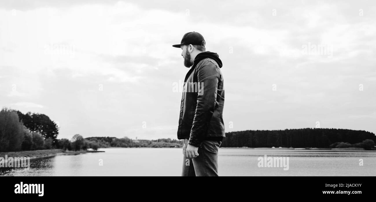 man in a leather jacket near the river stands and looks into the ...