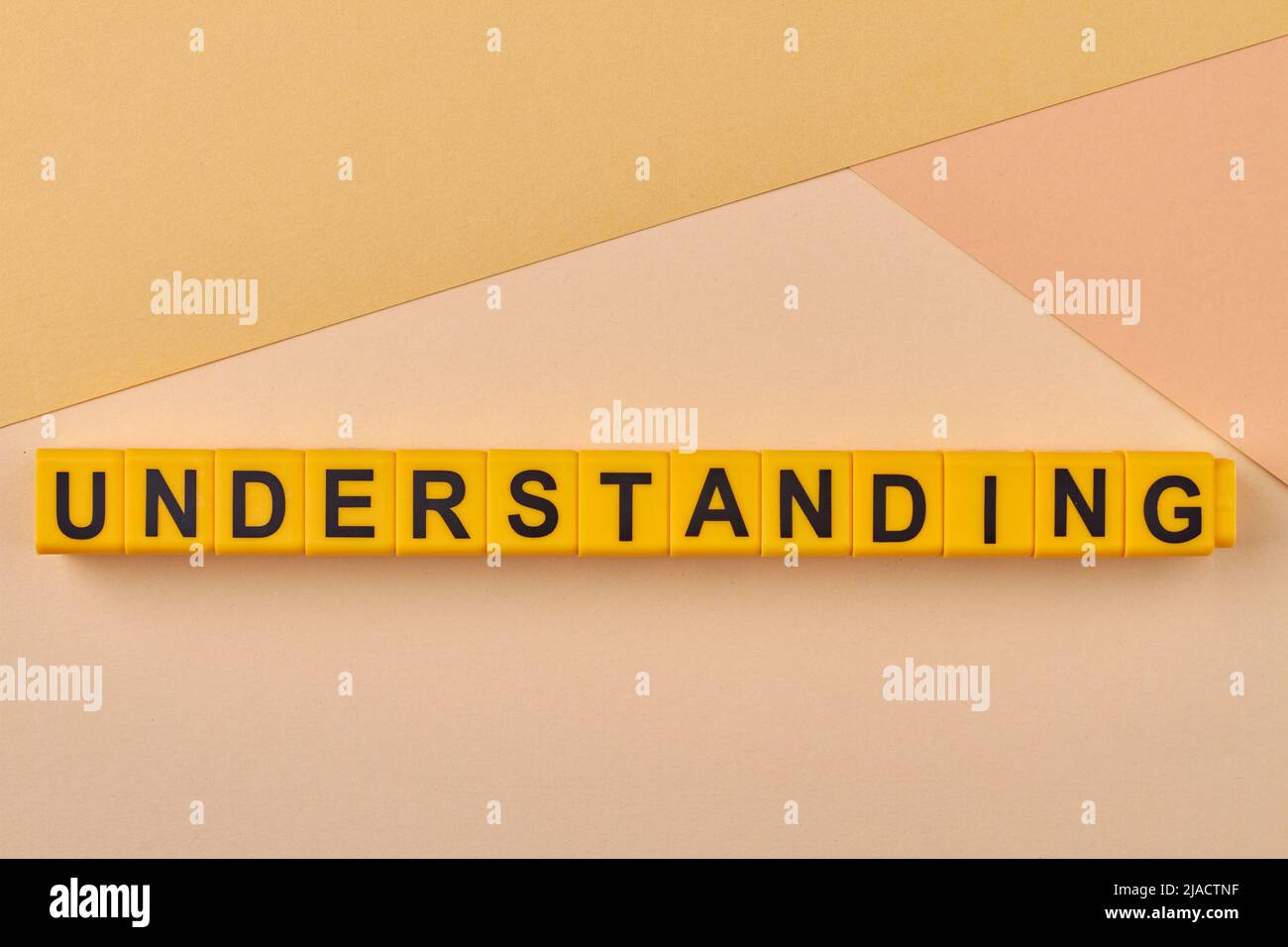 The word UNDERSTANDING written on yellow cubes against light background. Sympathetic awareness or tolerance. The ability to understand something. Stock Photo