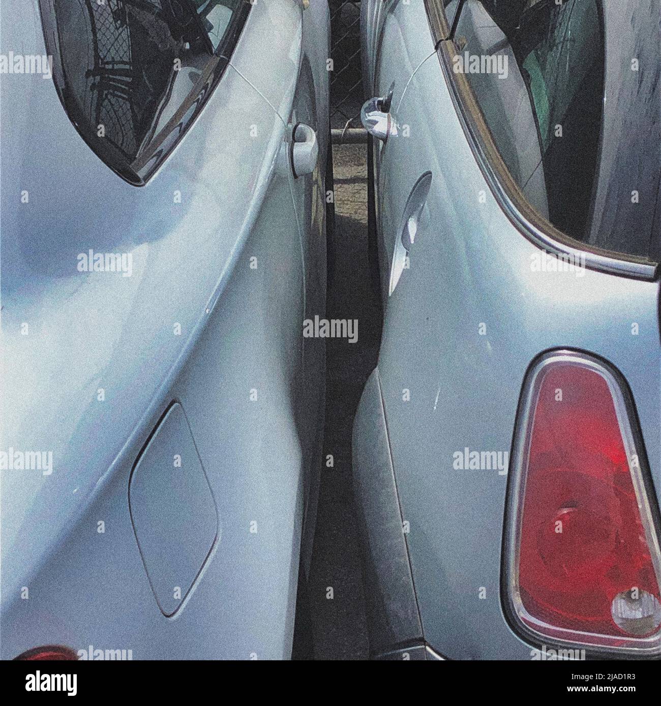 Outside an auto / car repair garage, two cars have been squeezed together with little chance of passengers or drivers exiting their vehicles. Stock Photo