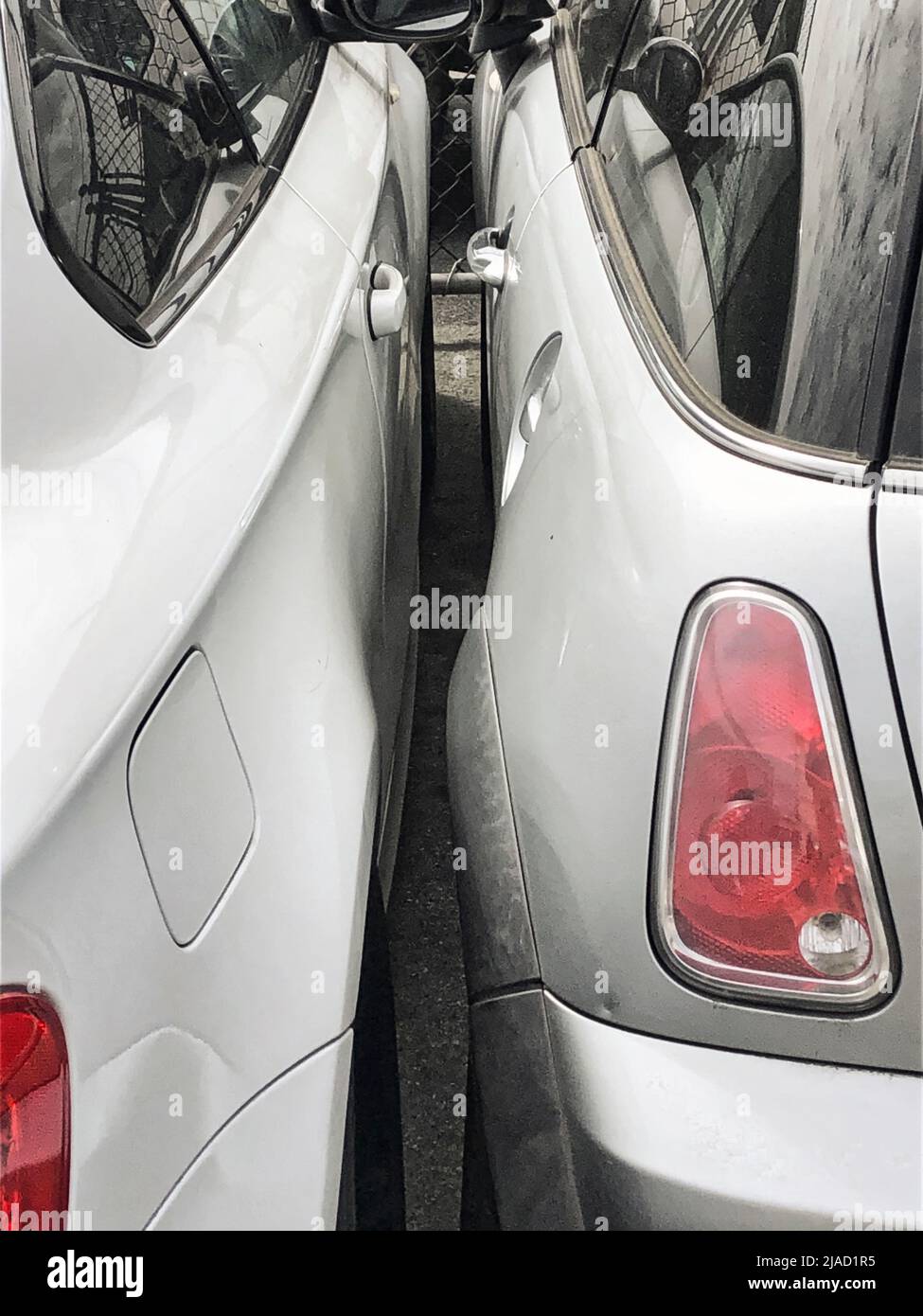 Outside an auto / car repair garage, two cars have been squeezed together with little chance of passengers or drivers exiting their vehicles. Stock Photo