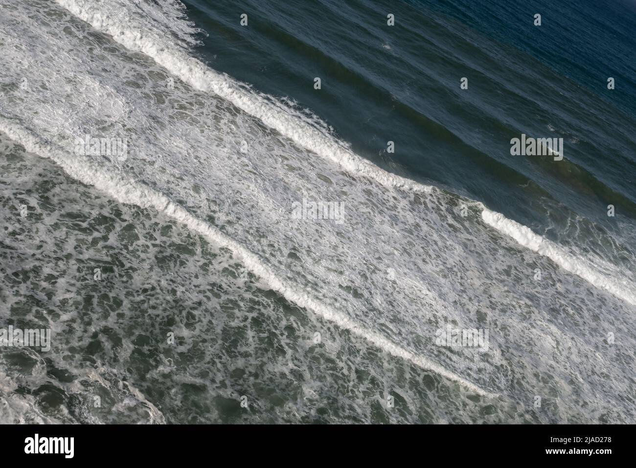 Rolling waves breaking near the Atlantic coast of Portugal in a regular diagonal pattern with white foam forming Stock Photo