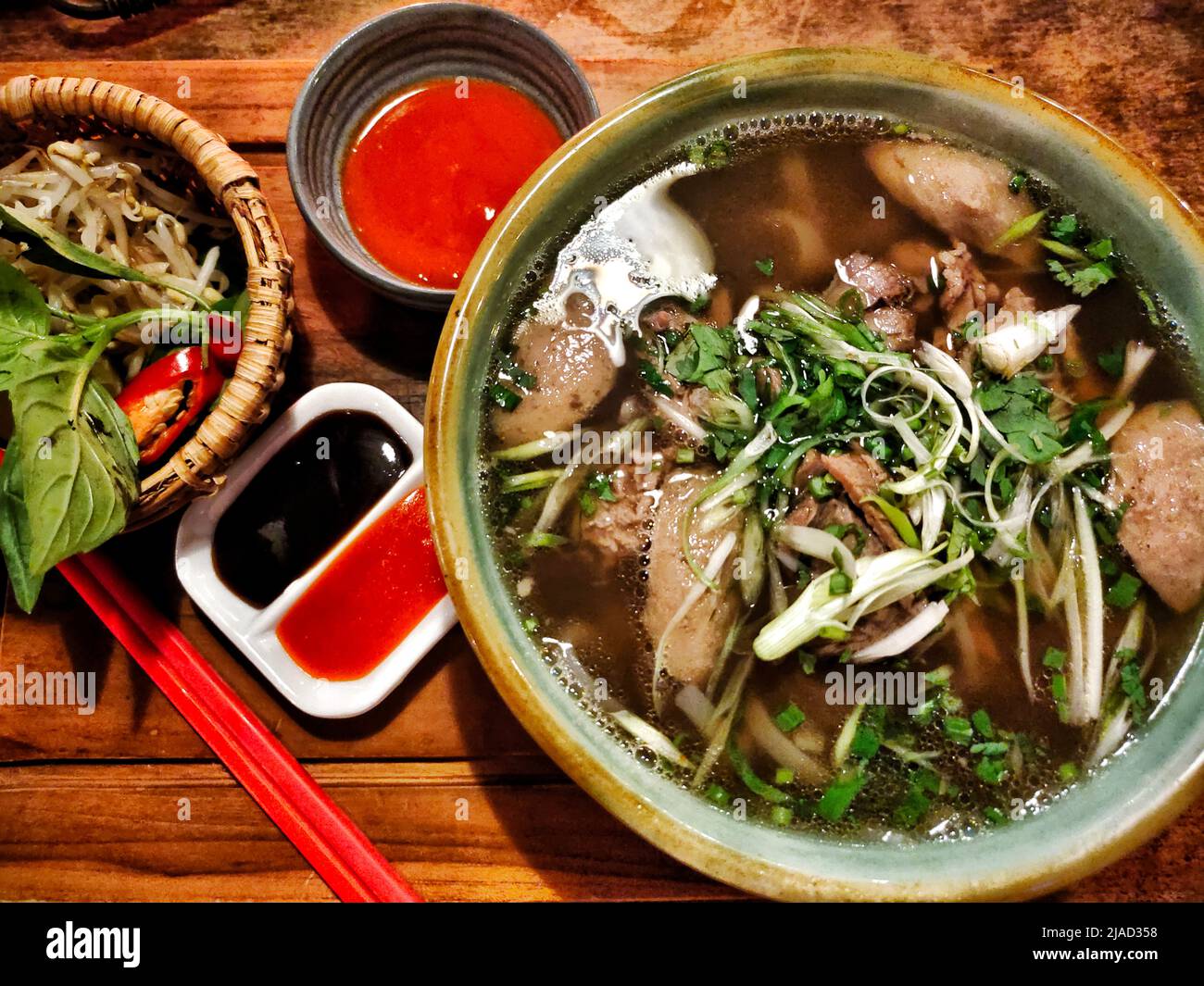Overhead view of a bowl of Vietnamese pho and assorted chili sauces