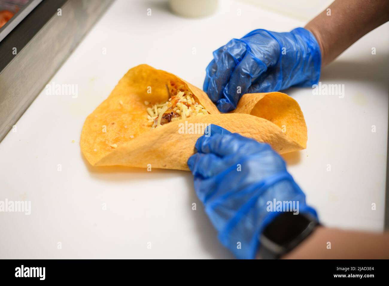 Close-Up of a person wearing disposable protective gloves preparing a tortilla wrap with chicken, cheese, onion and chili sauce Stock Photo