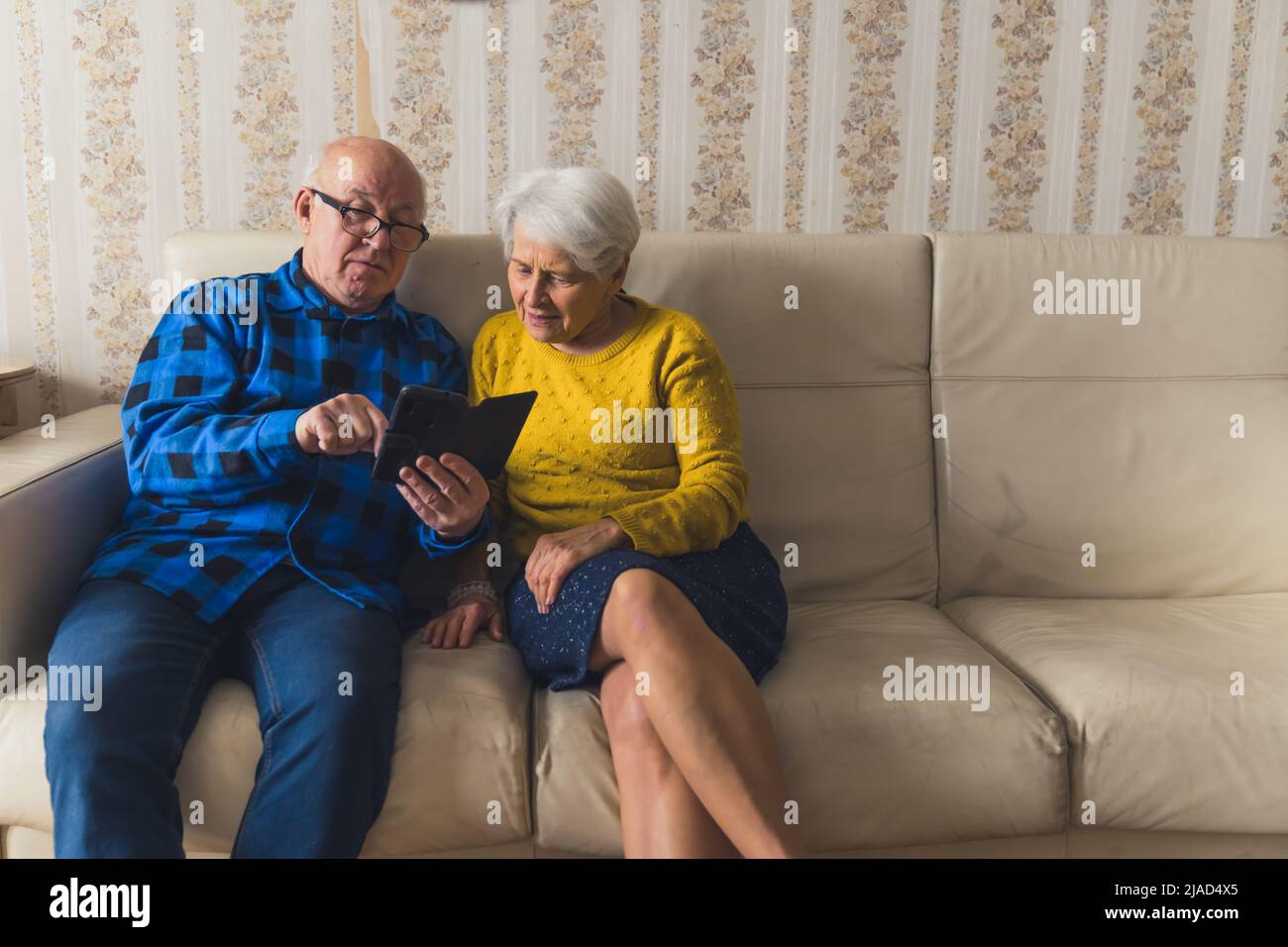 senior Eurpean couple sitting on the coach and watching something on the phone medium full shot indoor modern technology and senior people concept. High quality photo Stock Photo