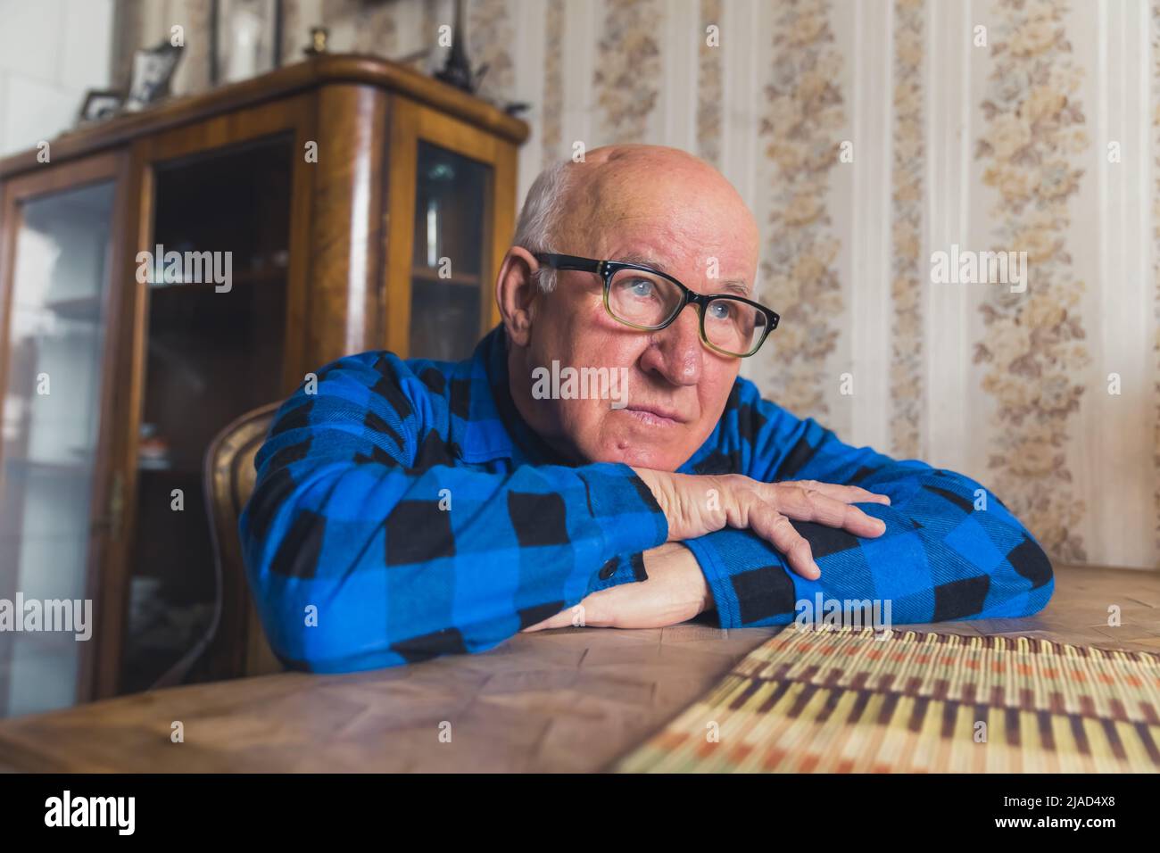 senior Caucasian man with glasses leaning on the table and looking ahead confidently medium closeup indoor senior people's problem concept. High quality photo Stock Photo