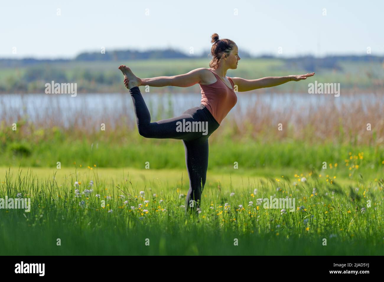 Woman standing on one leg doing dancer pose by Wallersee, Salzburg, Austria Stock Photo