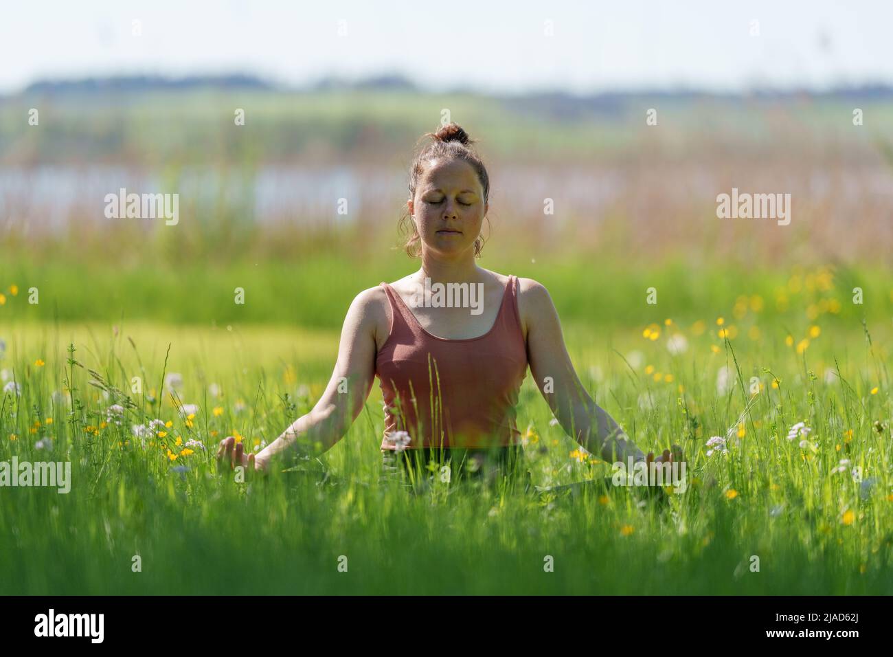 Woman sitting in lotus position meditating by Wallersee, Salzburg, Austria Stock Photo