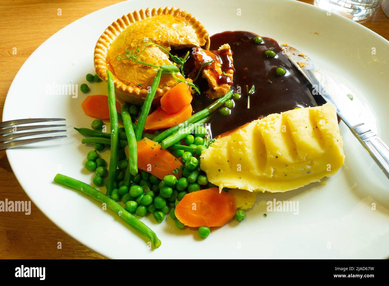 Tasty meal steak and ale pie cut open with mashed potatoes Tender Stem  broccoli carrots peas and gravy Stock Photo