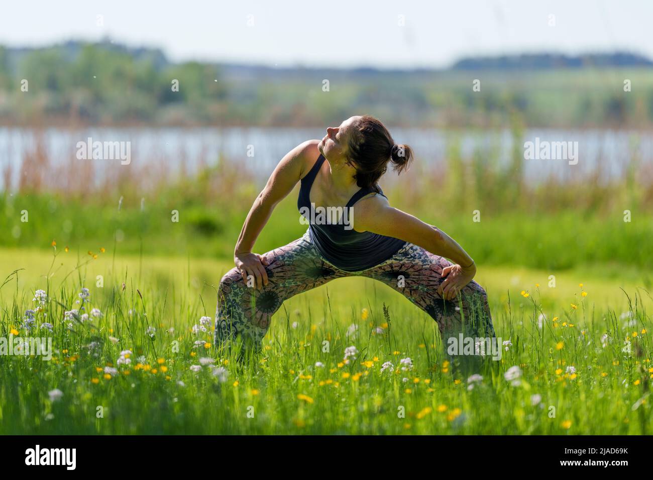 Woman doing standing cat cow yoga pose by Wallersee, Salzburg, Austria Stock Photo
