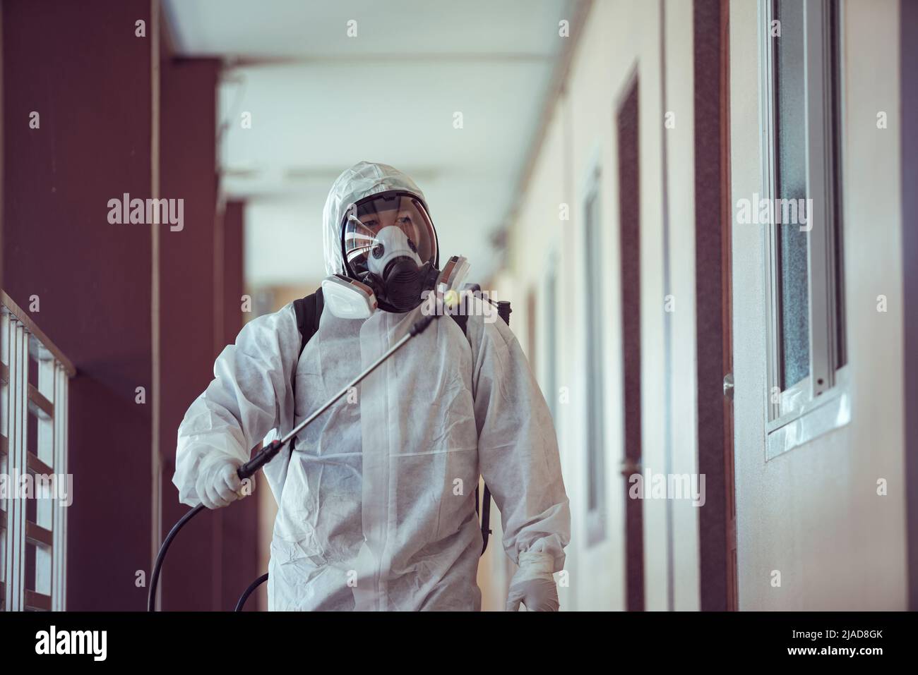 Cleaner in PPE spraying disinfectant inside a building Stock Photo