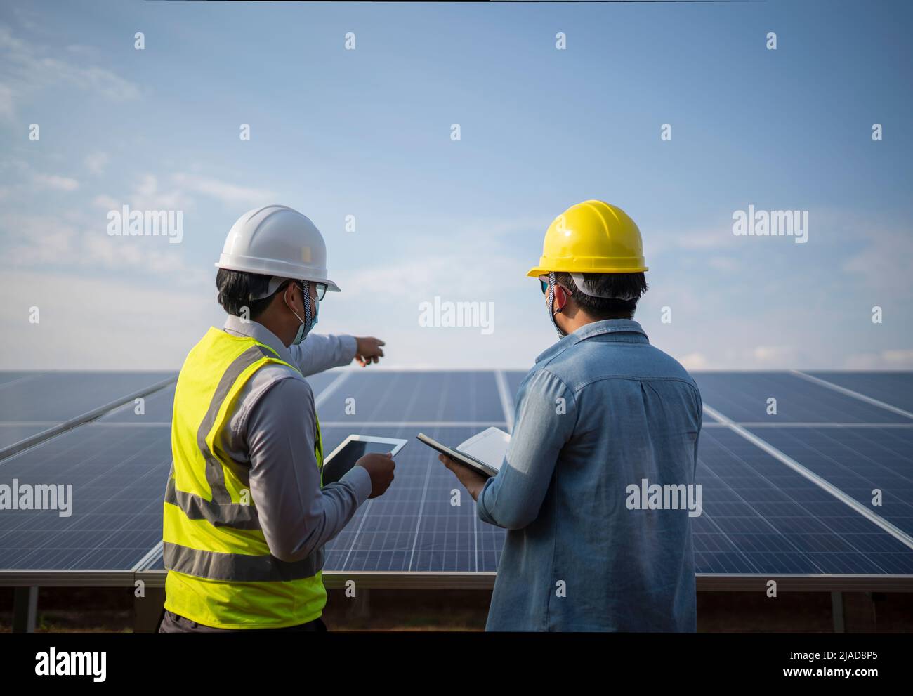 Two engineers standing next to solar panels at a solar powered station talking, Thailand Stock Photo