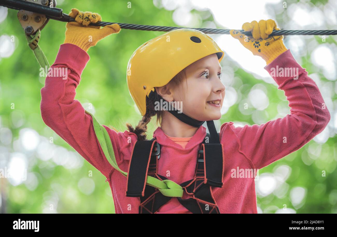 Portrait of a beautiful kid on a rope park among trees. Happy child in summer. Roping park. Rope park - climbing center. Toddler age. Kid climbing Stock Photo