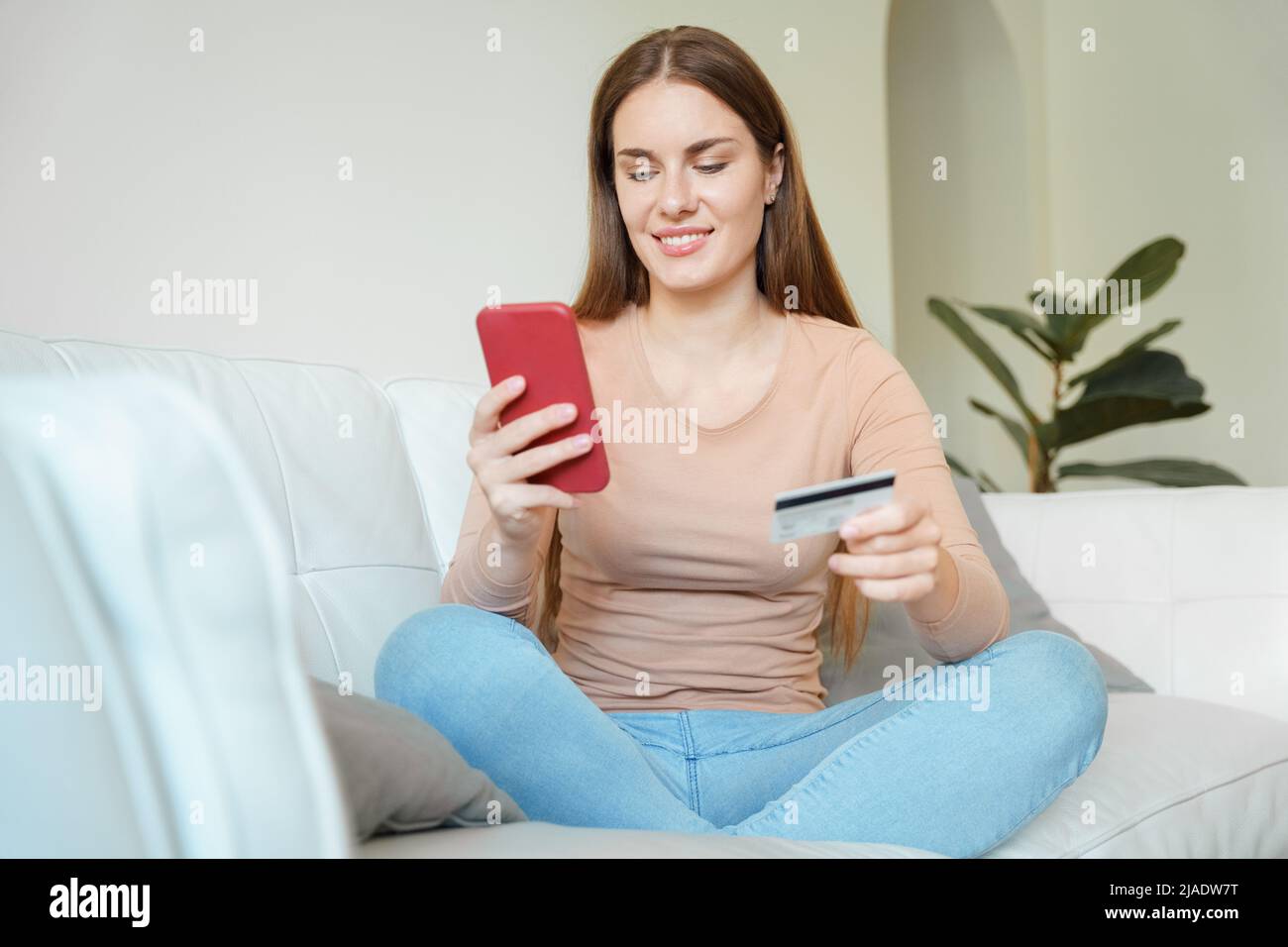 Young teenager woman doing online purchase using phone and credit card at home Stock Photo