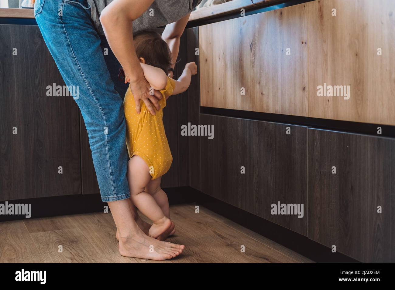 Mother picking up the angry baby standing at her feet. Mother and her baby. Stock Photo