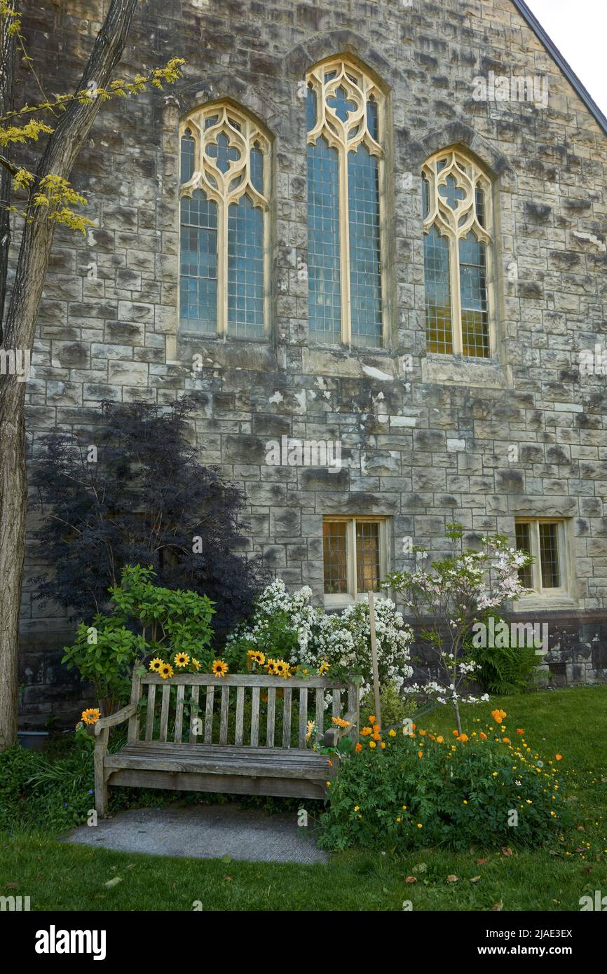 Empty wooden bench and spring flowers in the garden of Ryerson United Church in Kerrisdale, Vancouver, BC, Canada Stock Photo