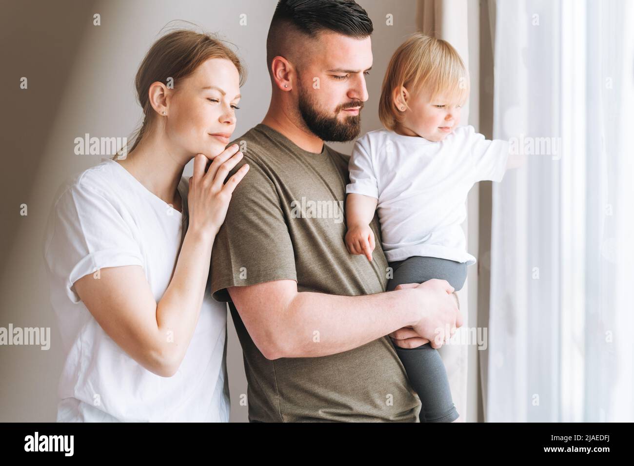 Happy multinational family father young man and mother with baby girl little daughter having fun near window room at home Stock Photo
